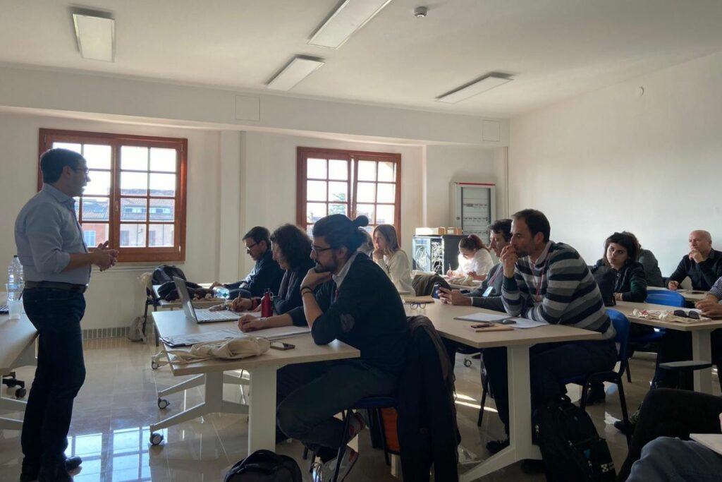 Alcune persone sedute in un aula ascoltano un insegnante.