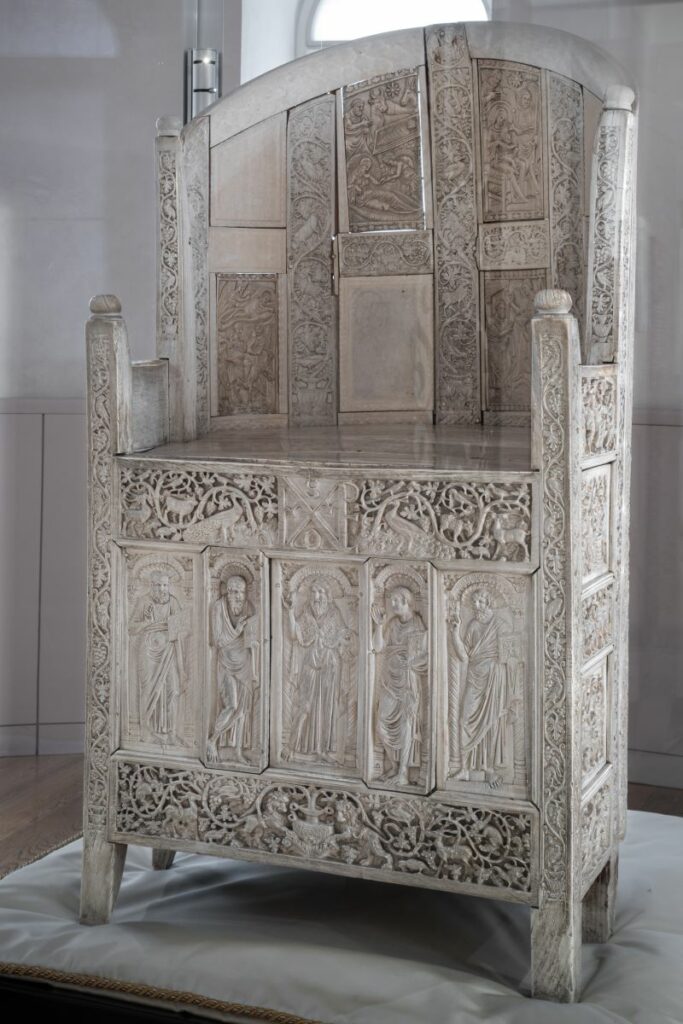 Foto della Cattedra d'avorio di colore bianco con inserti scolpiti con figure umane e girali vegetali.